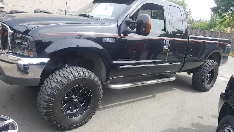 A gloss-black Ford F-350 lifted on black off-road wheels with mud-terrain tyres and chrome step bars, finished outside the shop.
